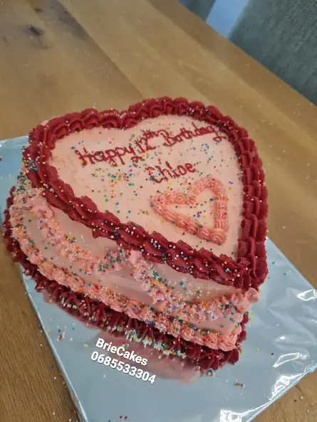 Pink heart-shaped birthday cake with red piping by Brie Cakes